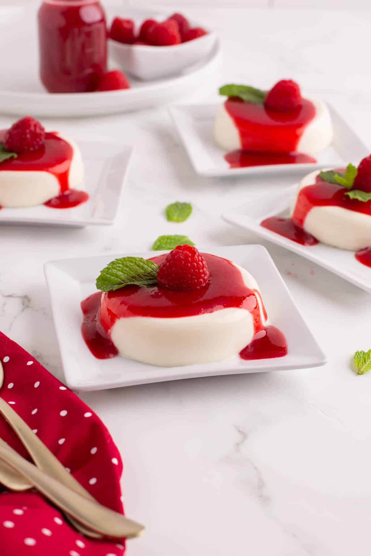 Servings of vanilla panna cotta with raspberry sauce on white plates.