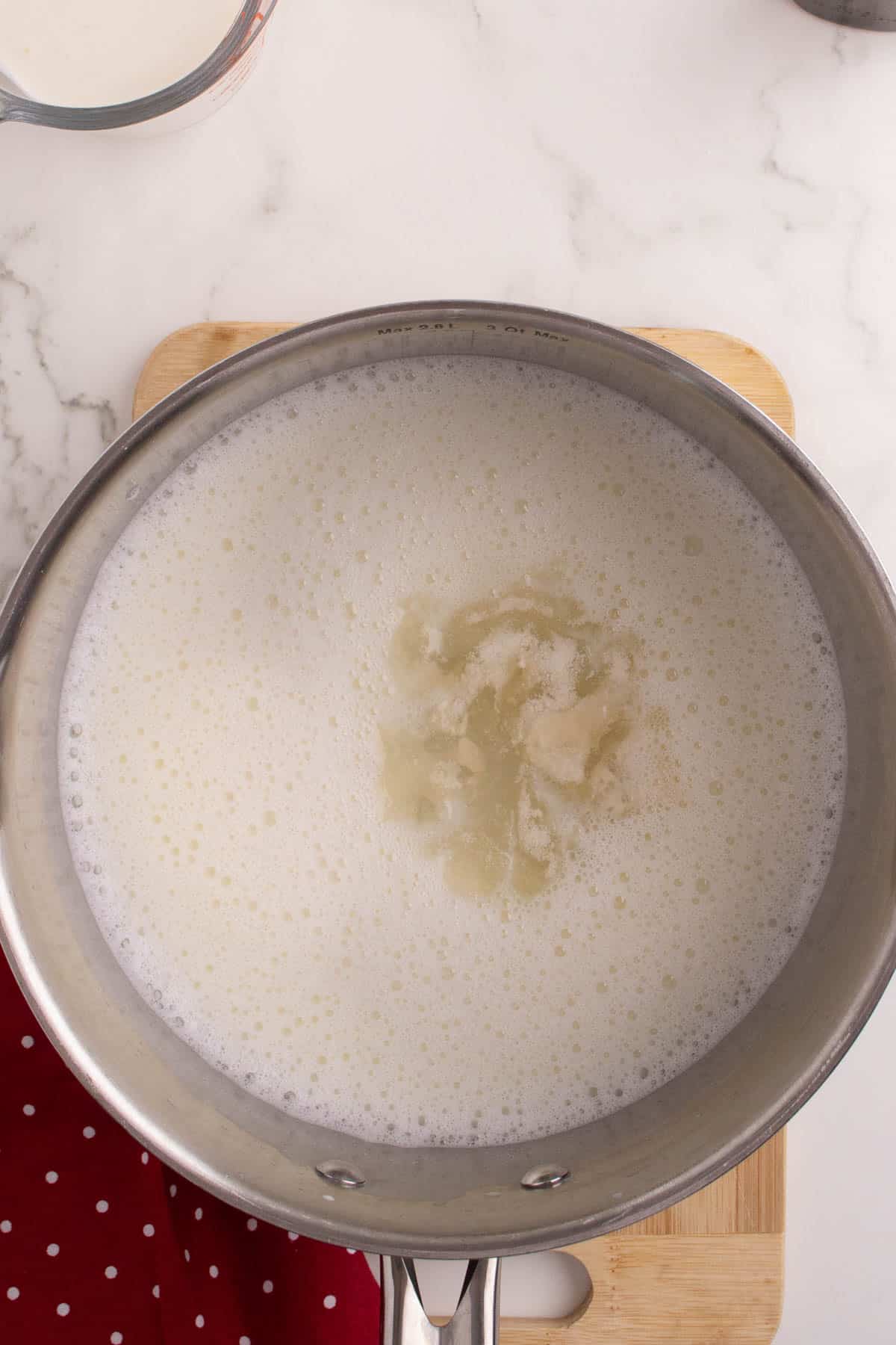 Adding dissolved gelatin to warm sugar and milk mixture in a pot.