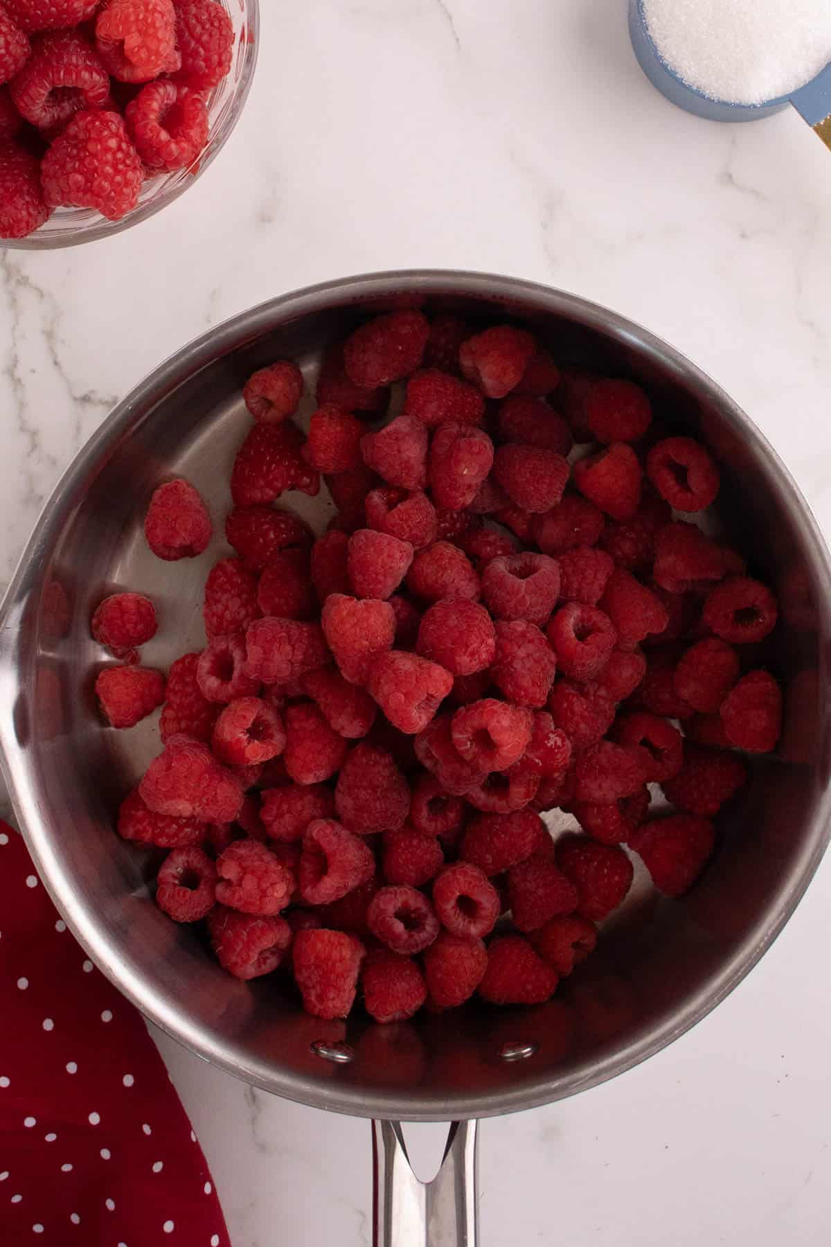 Combining raspberries and sugar in a saucepan.