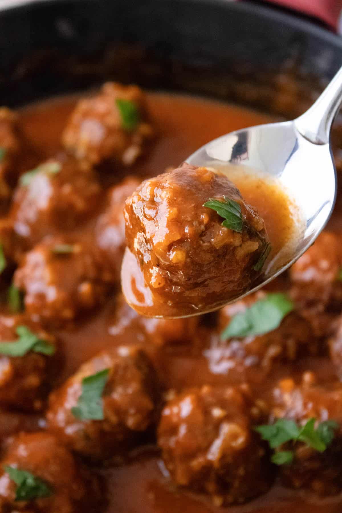 A spoon lifting a porcupine meatball out of the sauce.