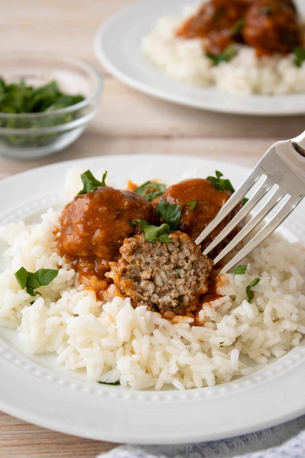 Porcupine meatballs on a plate of rice with a bite taken out of one of them.