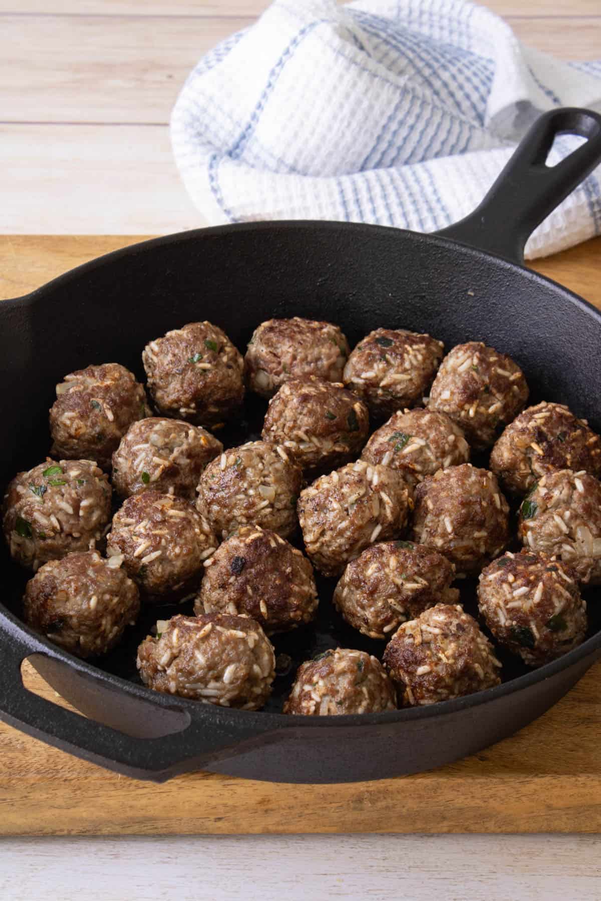 Browned porcupine meatballs in a large cast iron skillet.