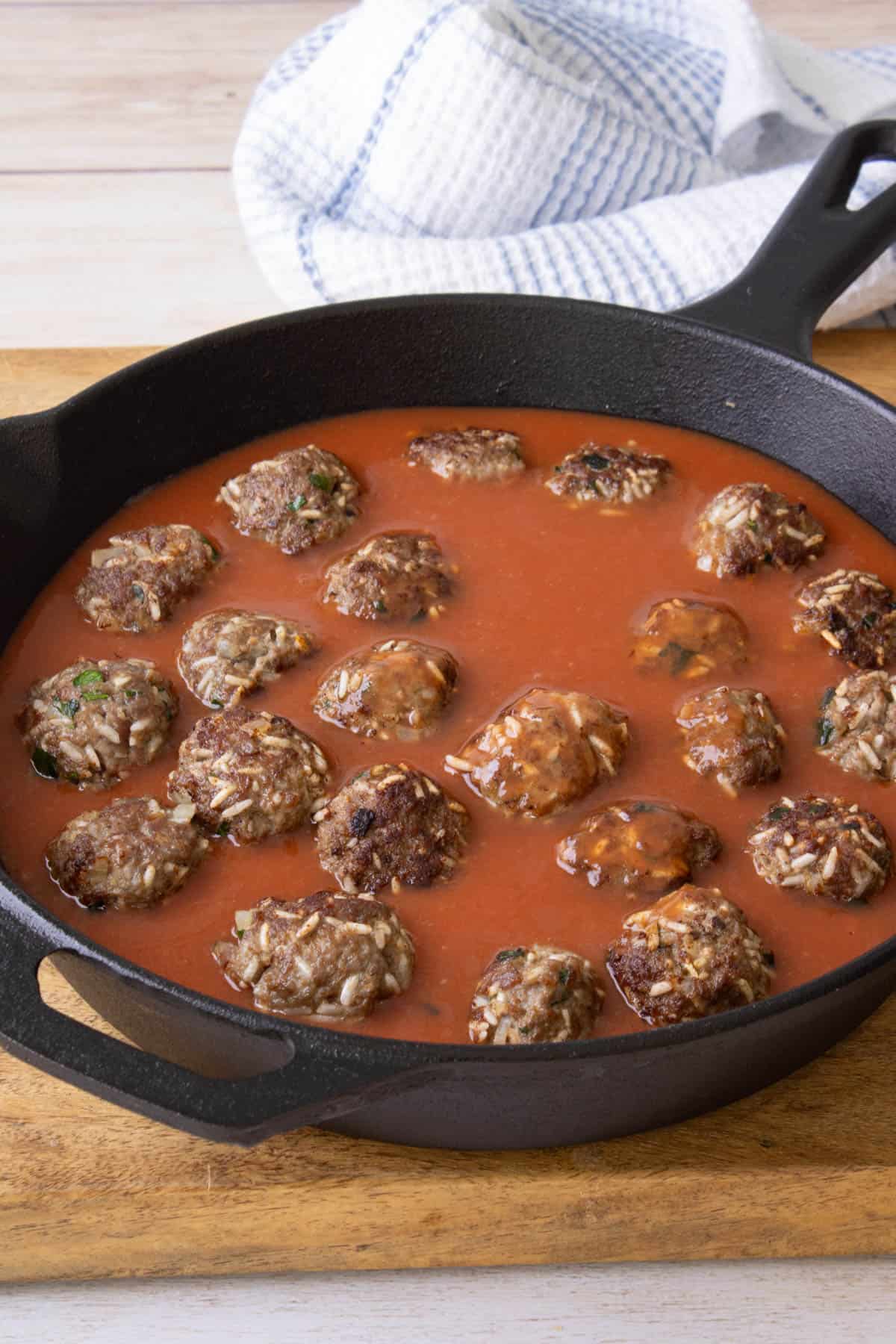 Adding sauce to browned porcupine meatballs in a large skillet.