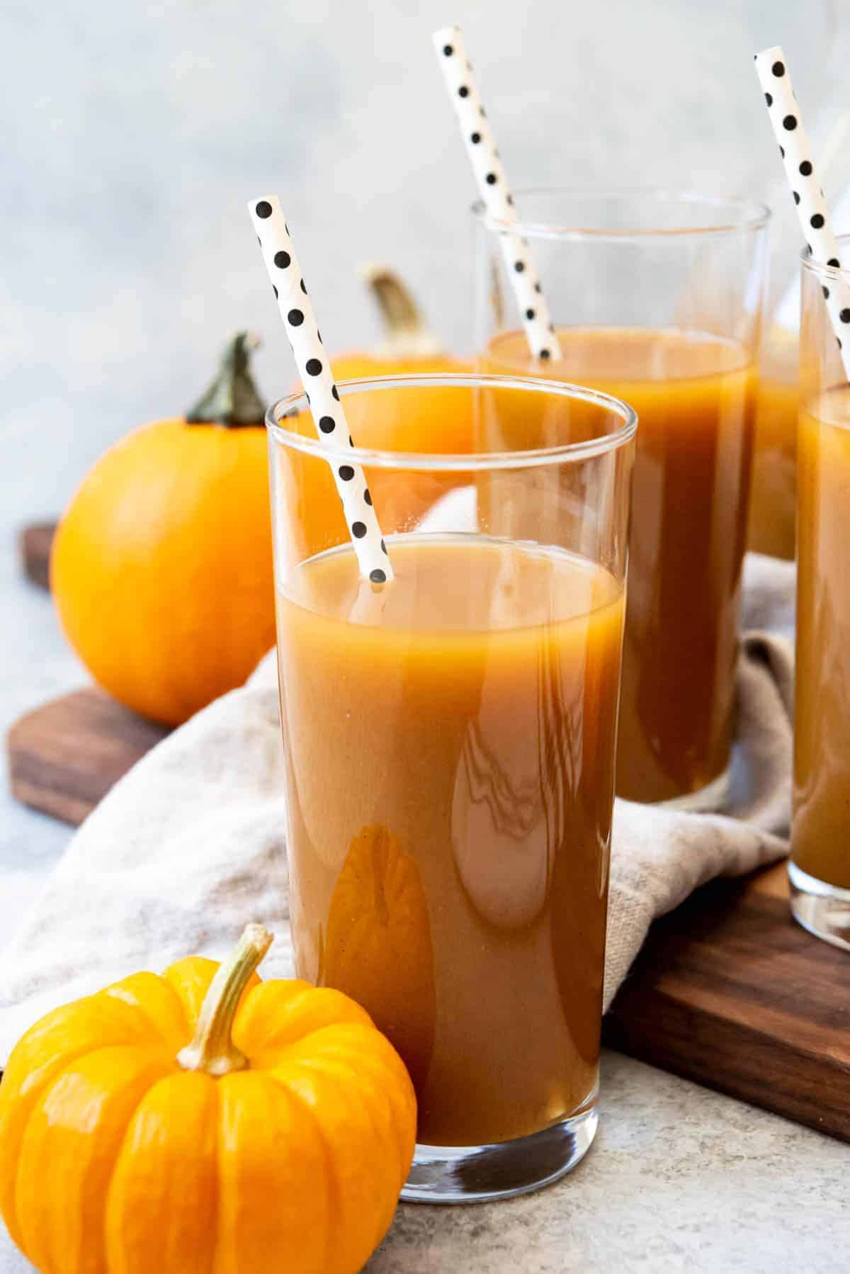 An image of Pumpkin juice in a tall glass with a polka dot straw.
