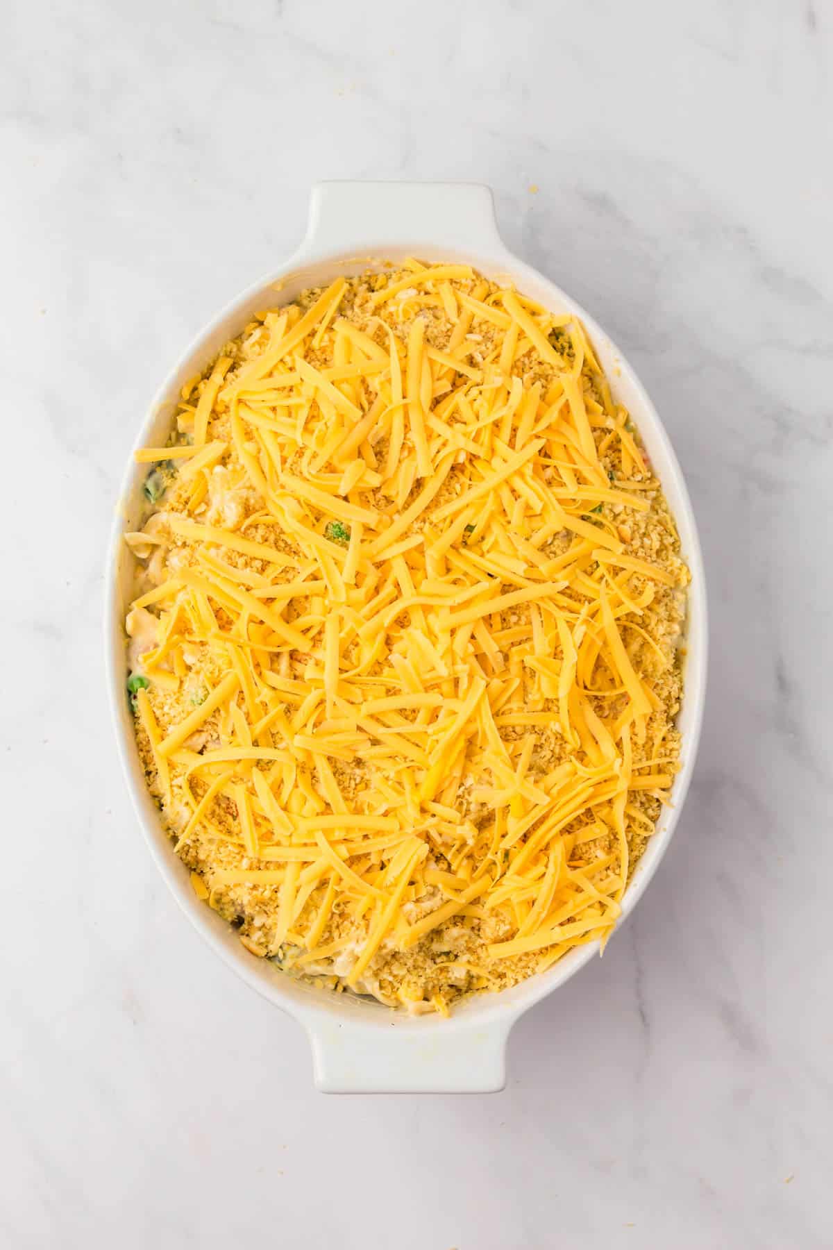 Sprinkling cheese over breadcrumbs in a baking dish.