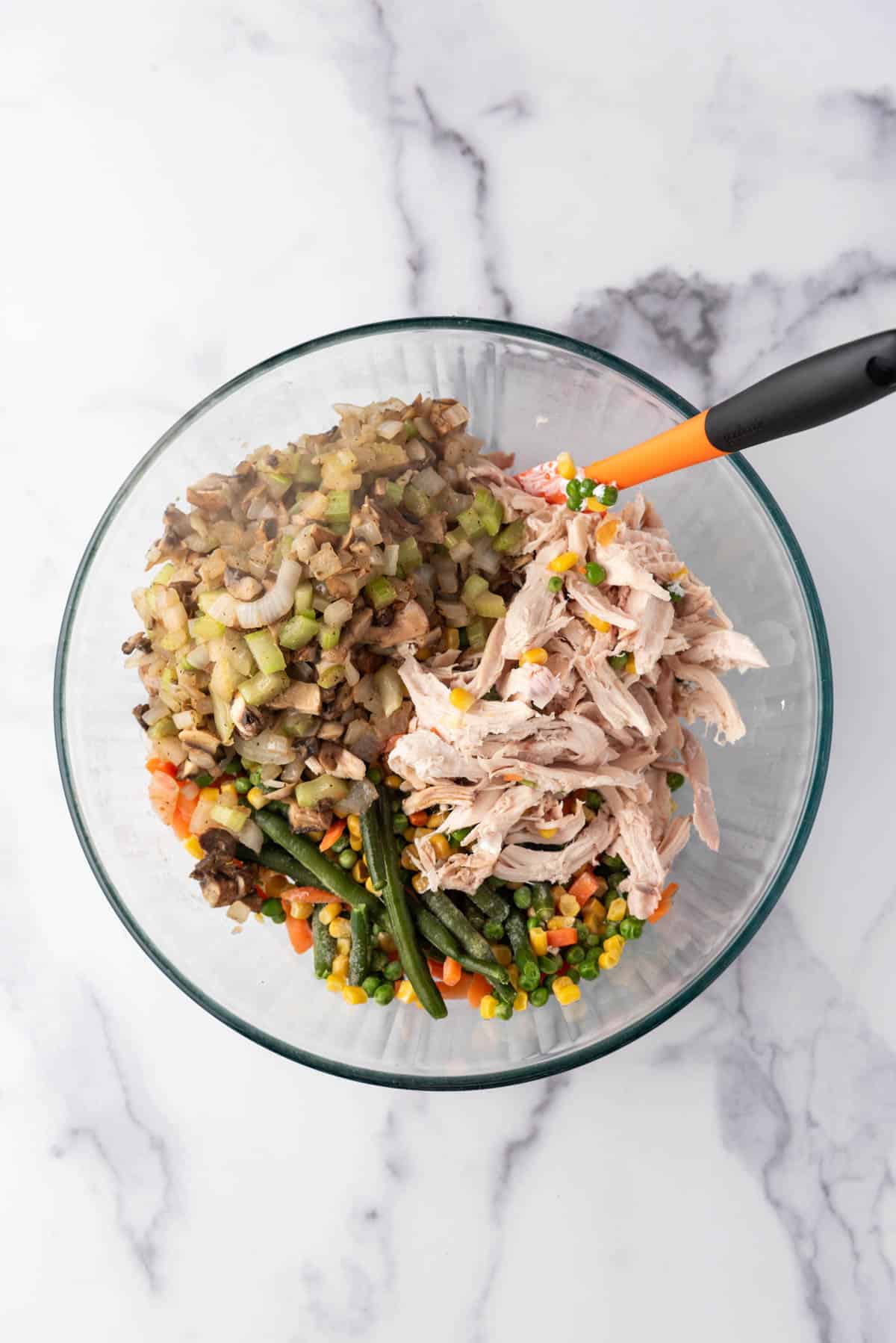 Combining shredded rotisserie chicken and vegetables in a large mixing bowl.