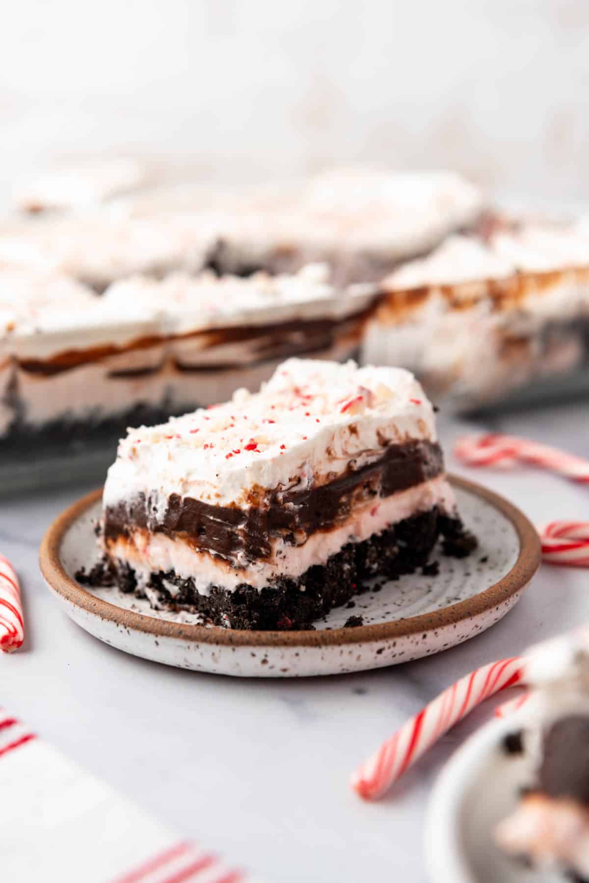 An image of chocolate peppermint lasagna on a plate with a candy cane next to it.