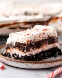 An image of chocolate peppermint lasagna on a plate with a candy cane next to it.