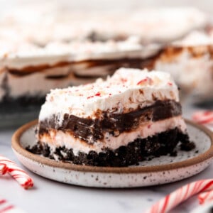 An image of chocolate peppermint lasagna on a plate with a candy cane next to it.