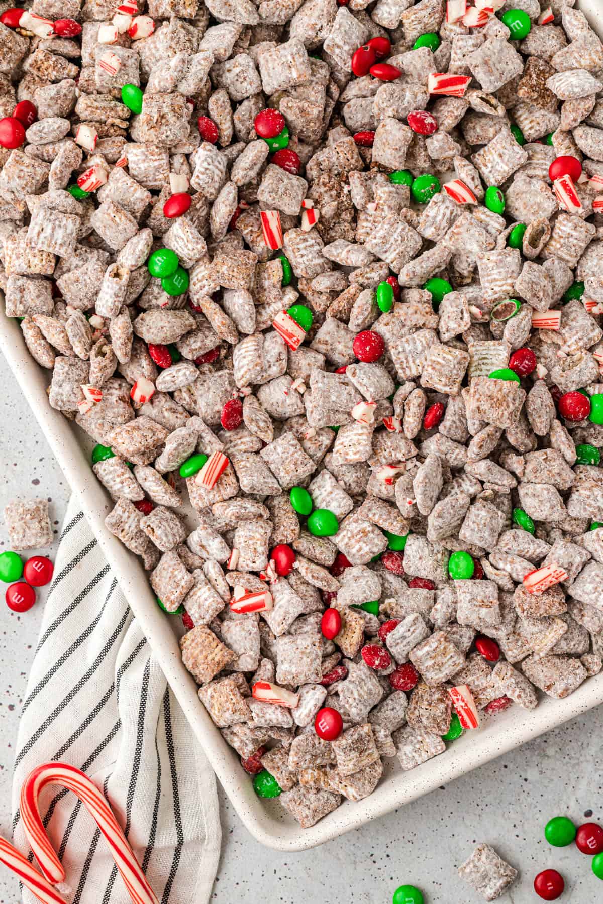 An overhead image of Christmas puppy chow with candy canes and M&Ms.