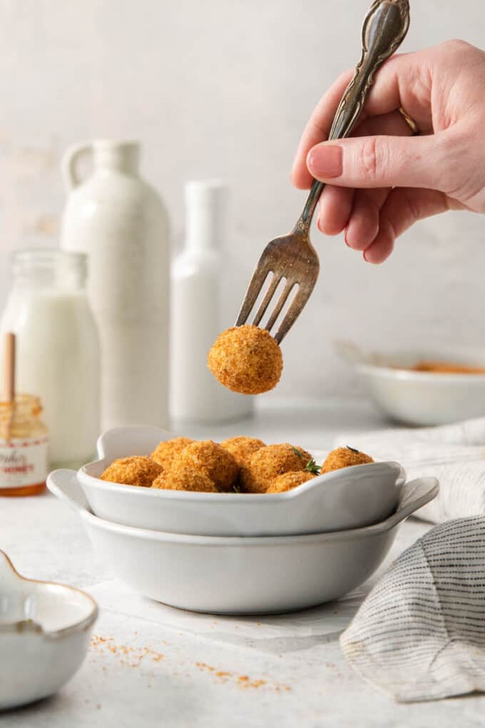 A fork lifting a crispy goat cheese bite out of a bowl.