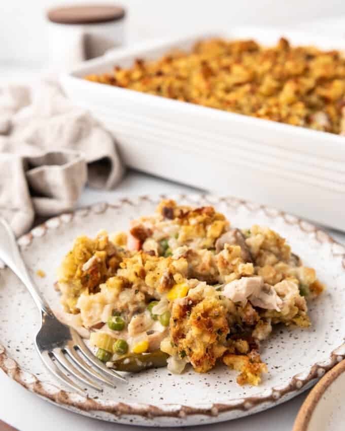 A scoop of chicken and stuffing casserole on a plate in front of the baking dish.