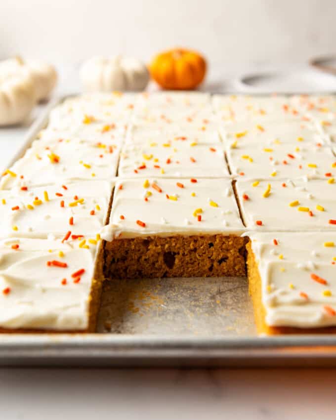An image of pumpkin sheet bars with cream cheese frosting with a piece taken out.