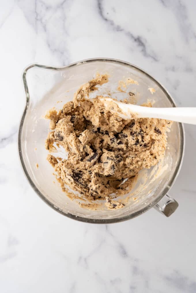 Mixing chocolate chip cookie dough in a large glass bowl.