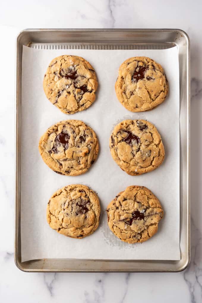 Six baked Jacques Torres chocolate chip cookies on a baking sheet lined with parchment paper.