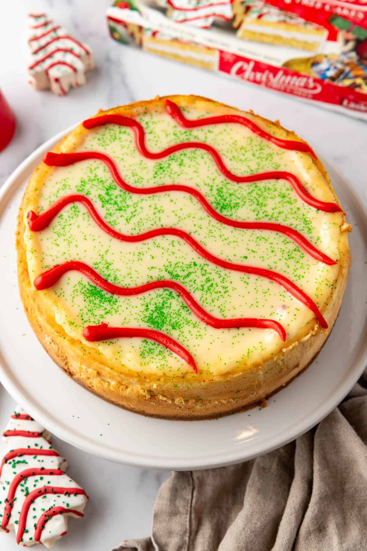 An unsliced Little Debbie Christmas Tree Cheesecake on a white cake plate.