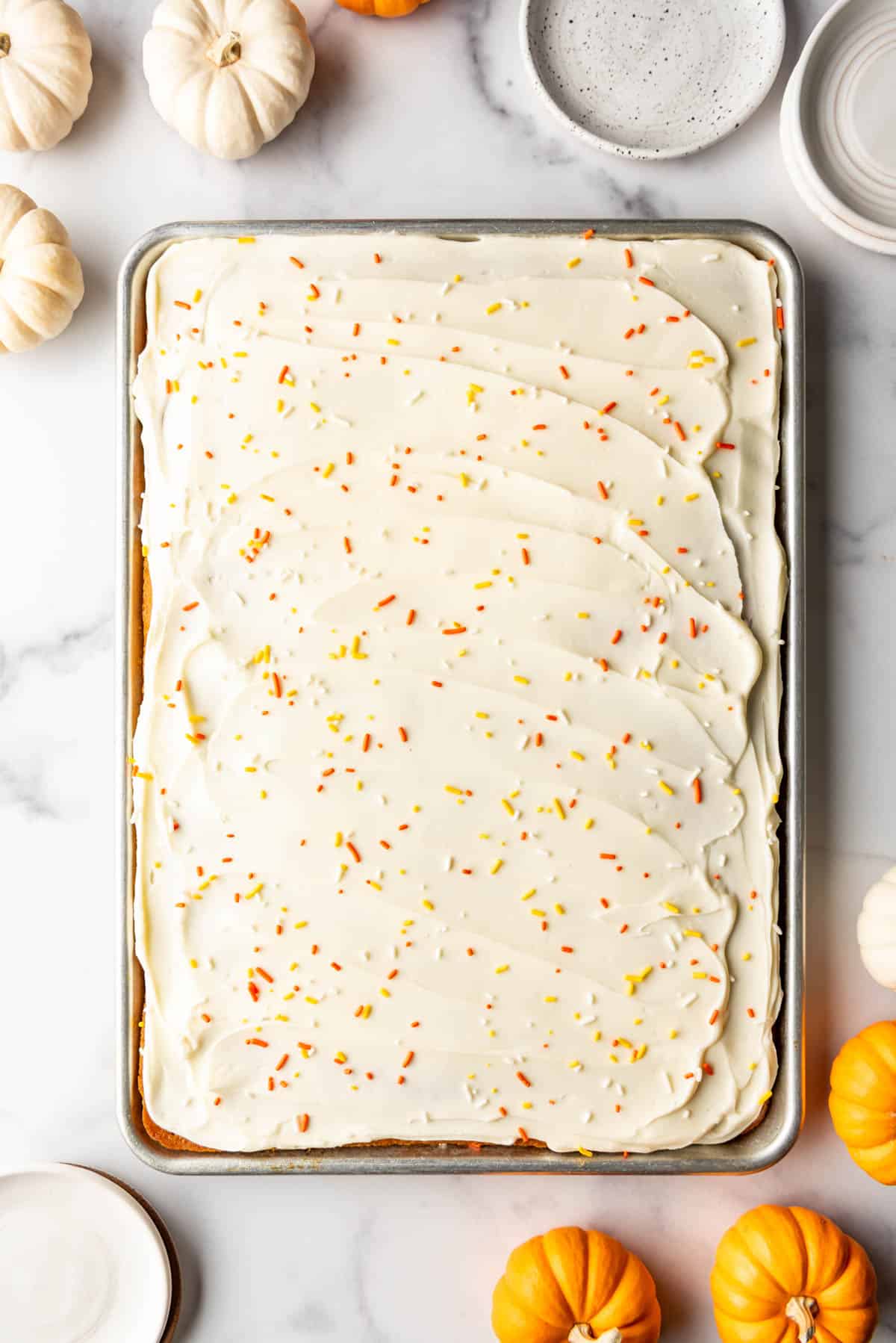 An image of frosted pumpkin sheet cake bars with mini pumpkins surrounding the pan.