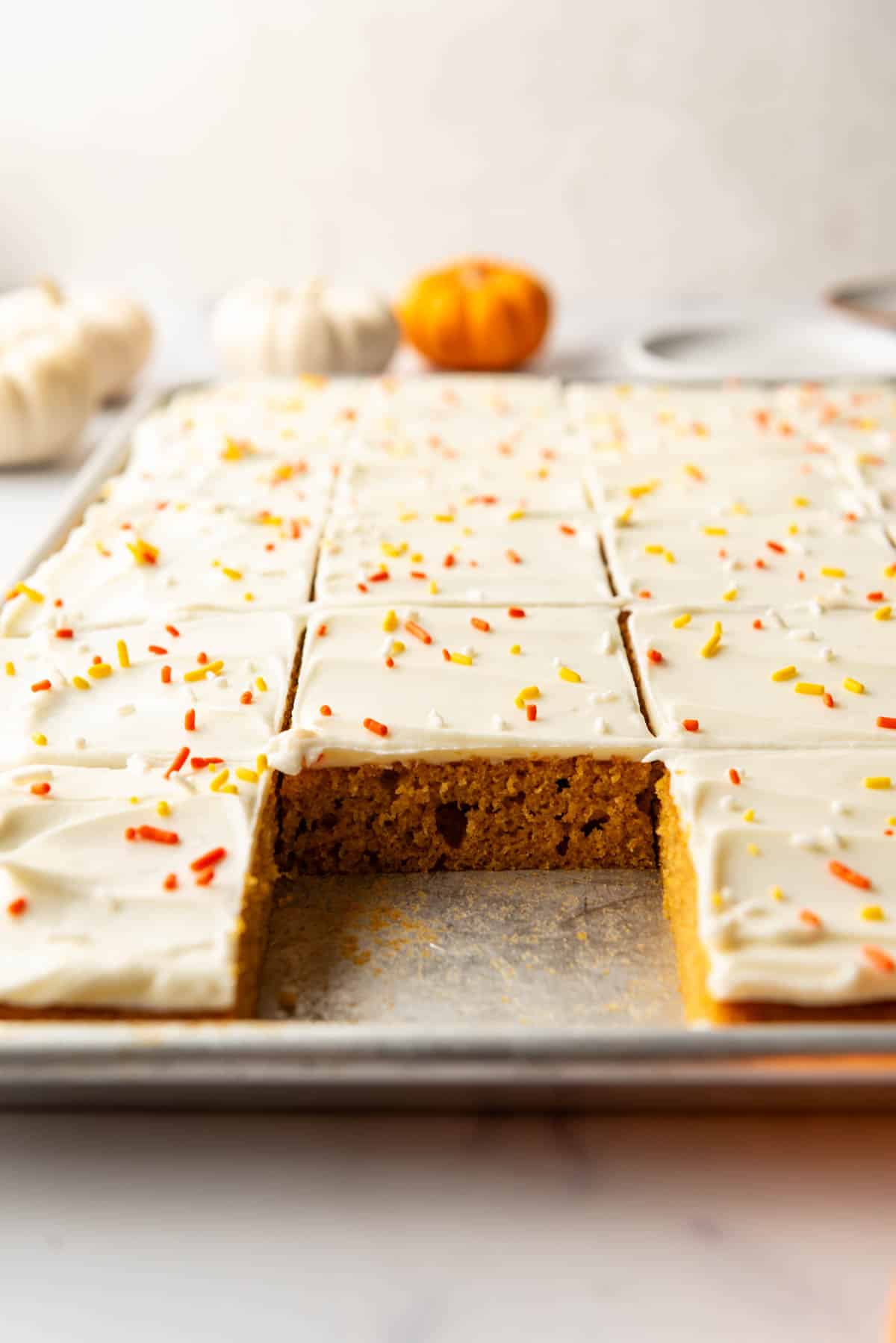 An image of pumpkin sheet bars with cream cheese frosting with a piece taken out. 