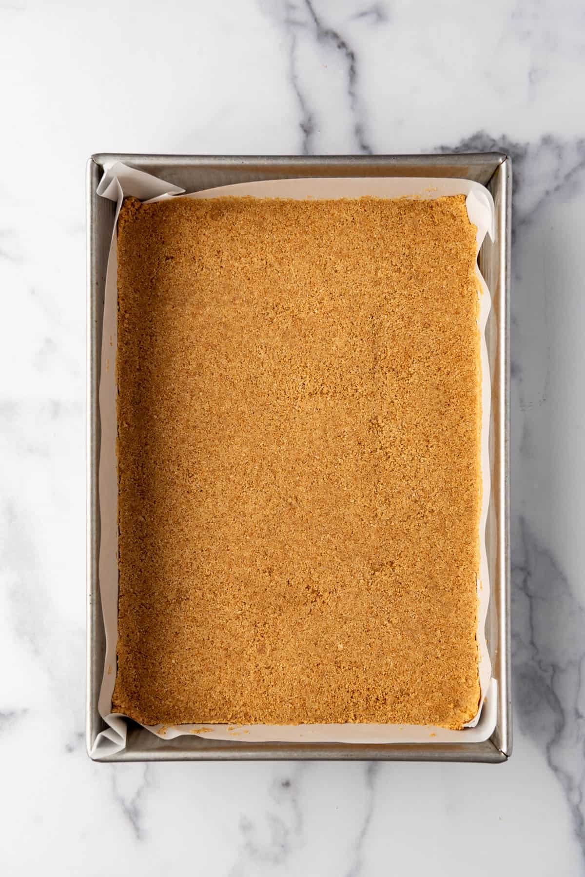 Pressing a graham cracker crust into a 9x13-inch baking dish.