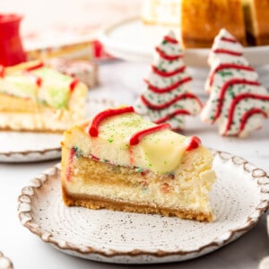 A slice of Little Debbie Christmas Tree Cheesecake on a plate in front of two of the holiday snack cakes.