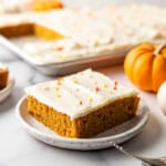 An image of a piece of a pumpkin bar on a plate with mini pumpkins in the background.