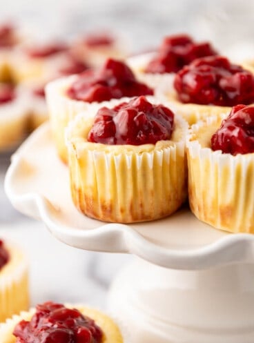 A close image of cherry cheesecake tarts on a white cake stand.