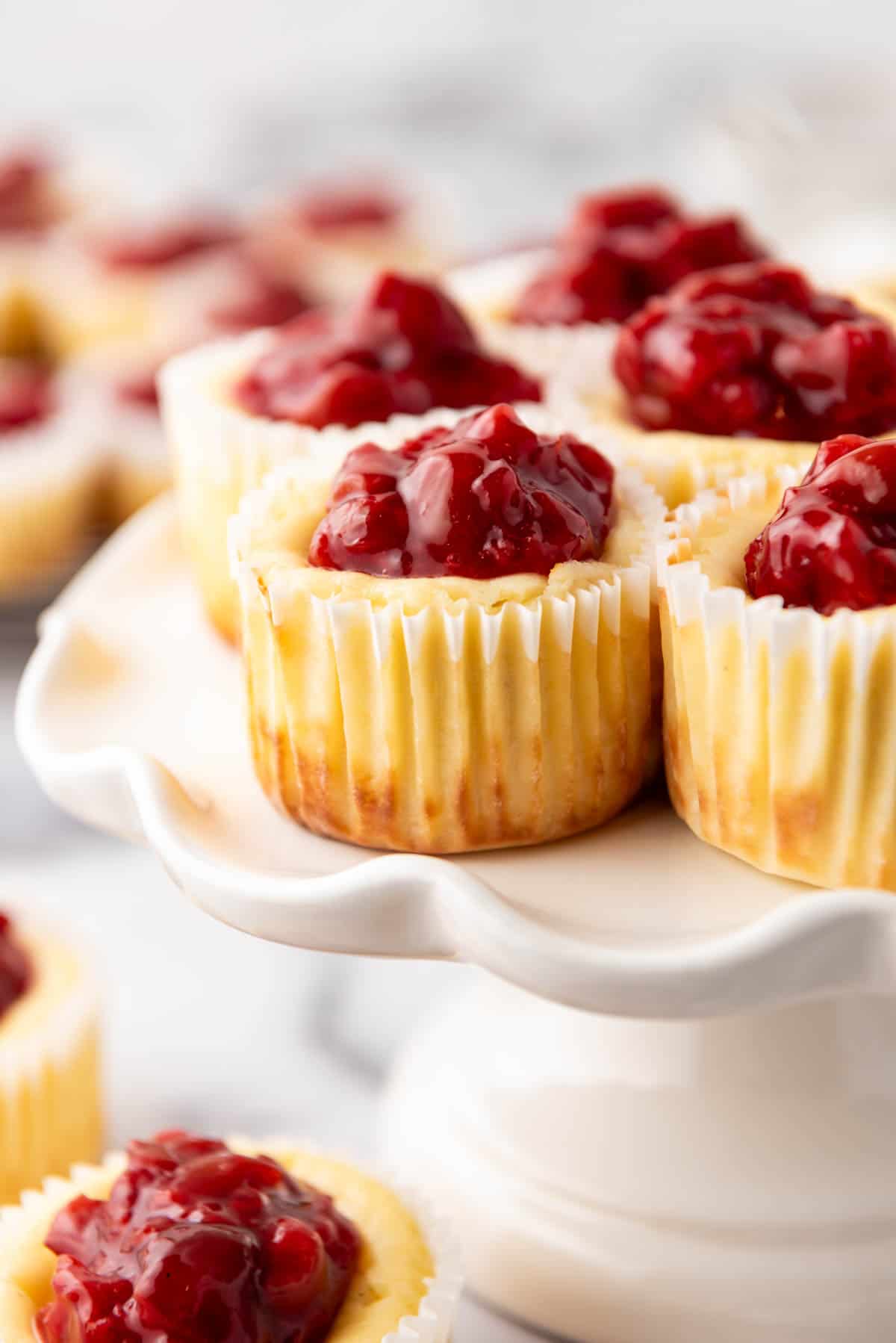 A close image of cherry cheesecake tarts on a white cake stand.