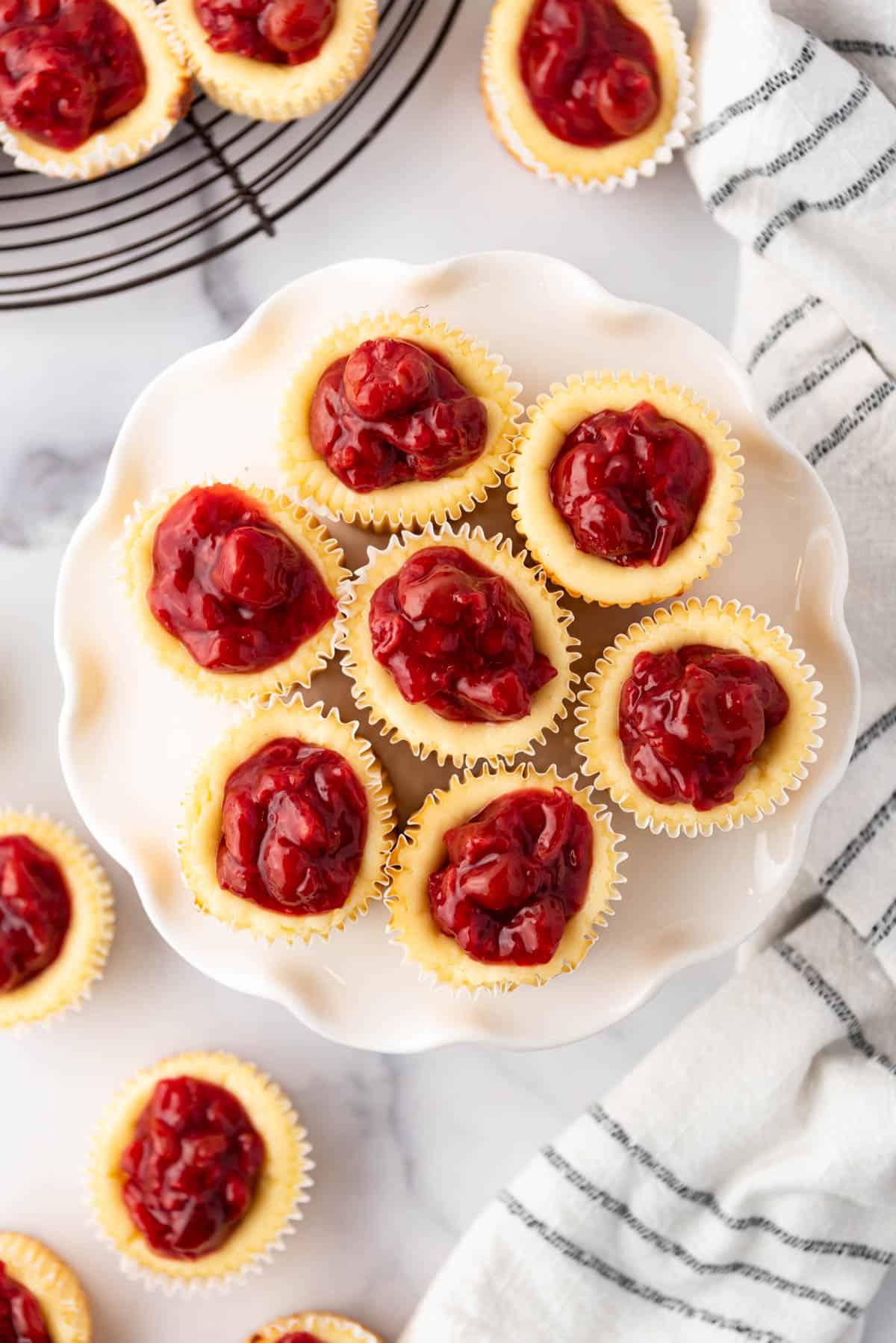 An overhead image of cherry cheesecake tarts on a white cake stand.