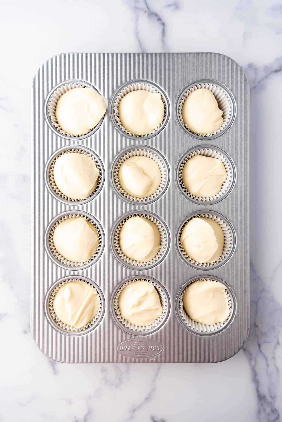 Adding cheesecake batter to muffin pans.