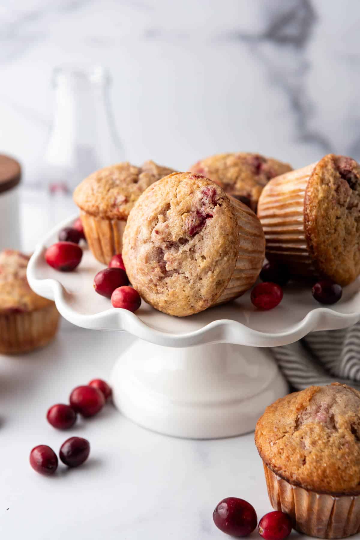 Leftover cranberry sauce muffins on a white cake stand with fresh cranberries scattered around.