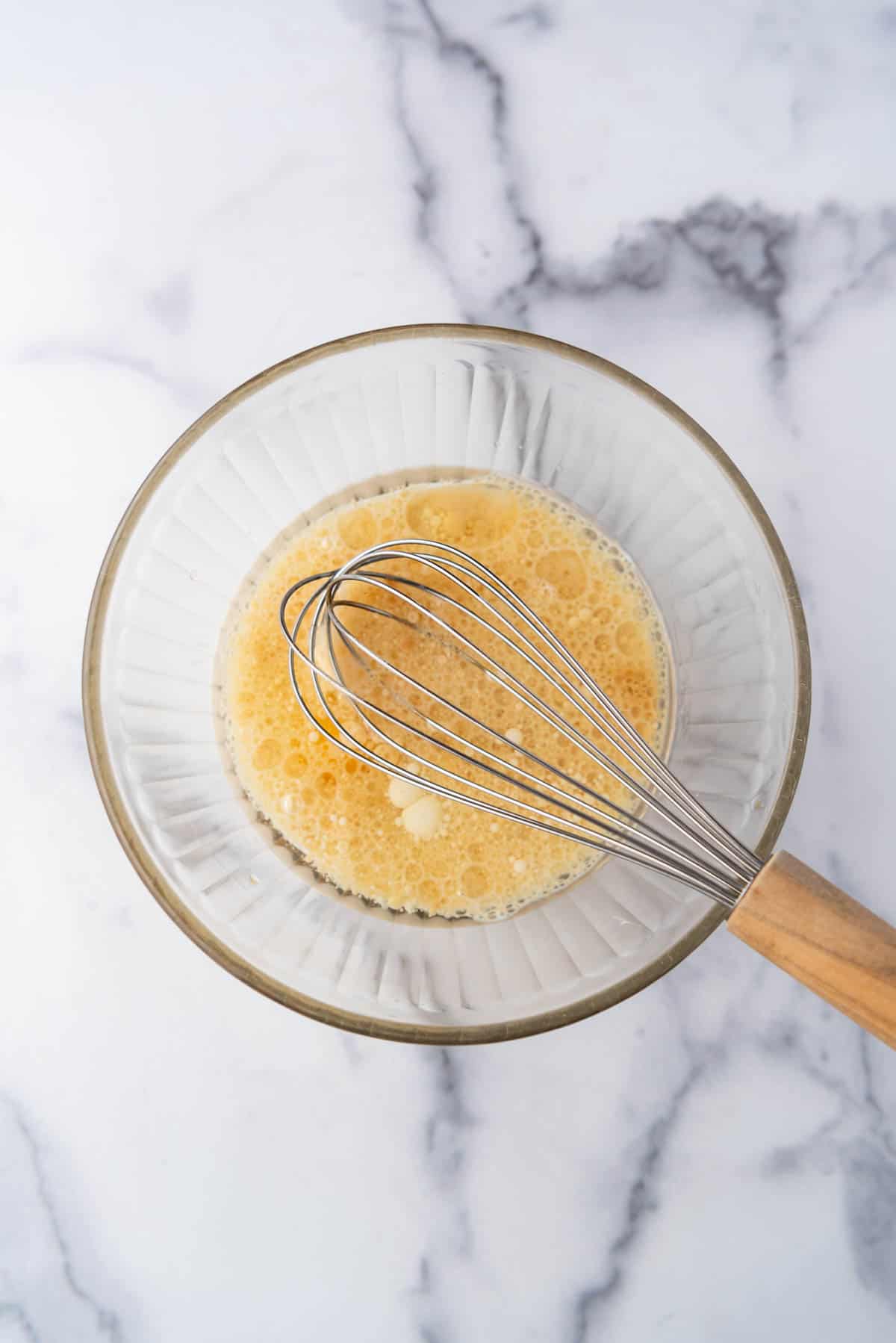 A whisk in a bowl of oil, egg, milk, and vanilla extract.