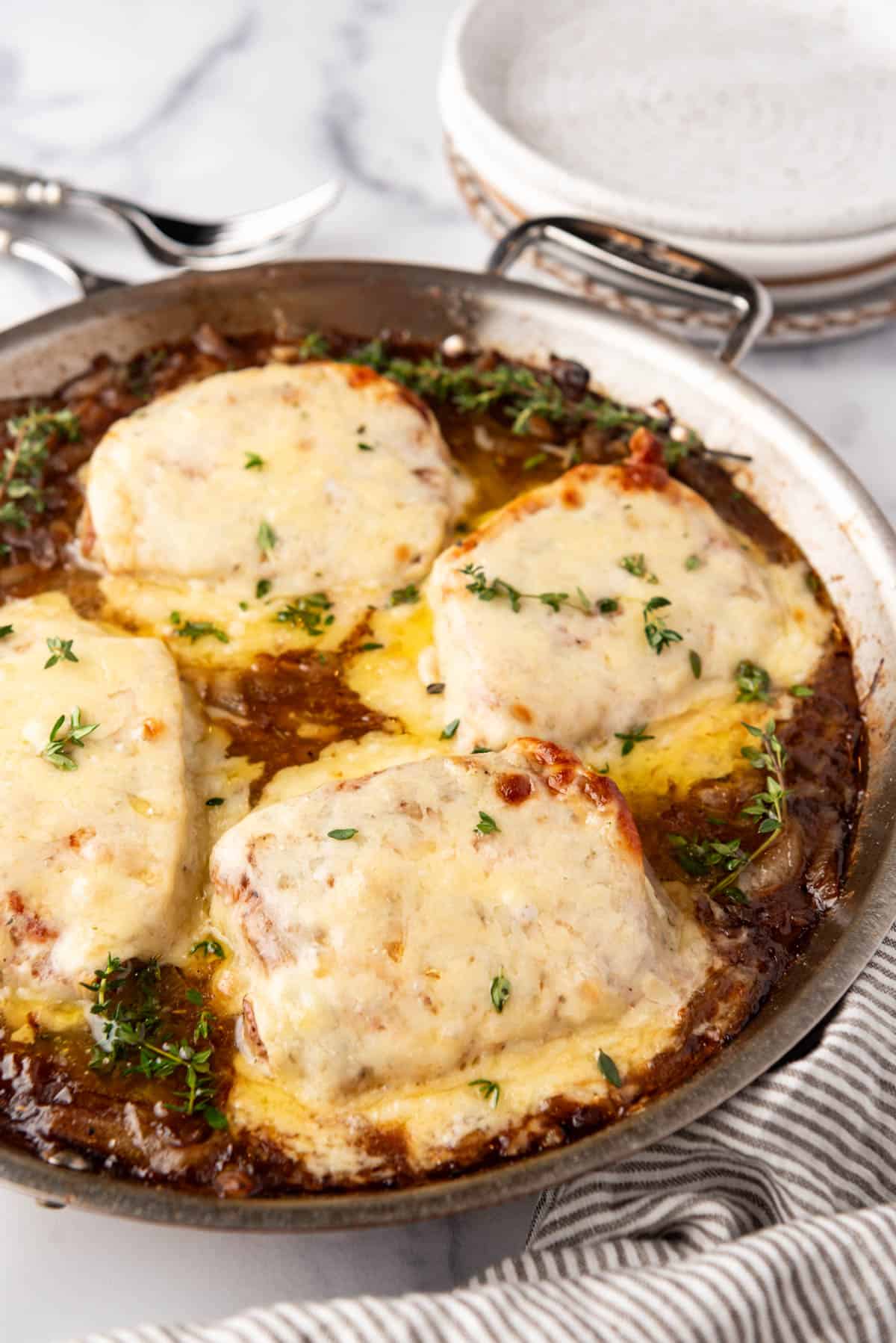 An image of four french onion pork chops in a pan with melted cheese on top.