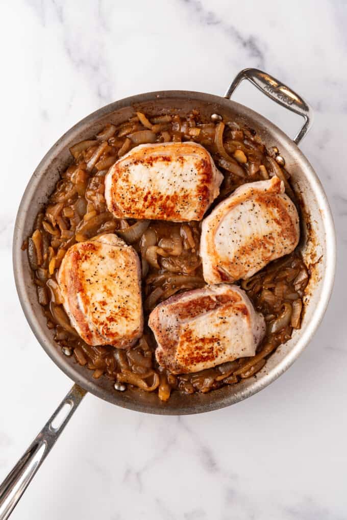 An overhead image of 4 browned pork chops in a pan with caramelized onions.