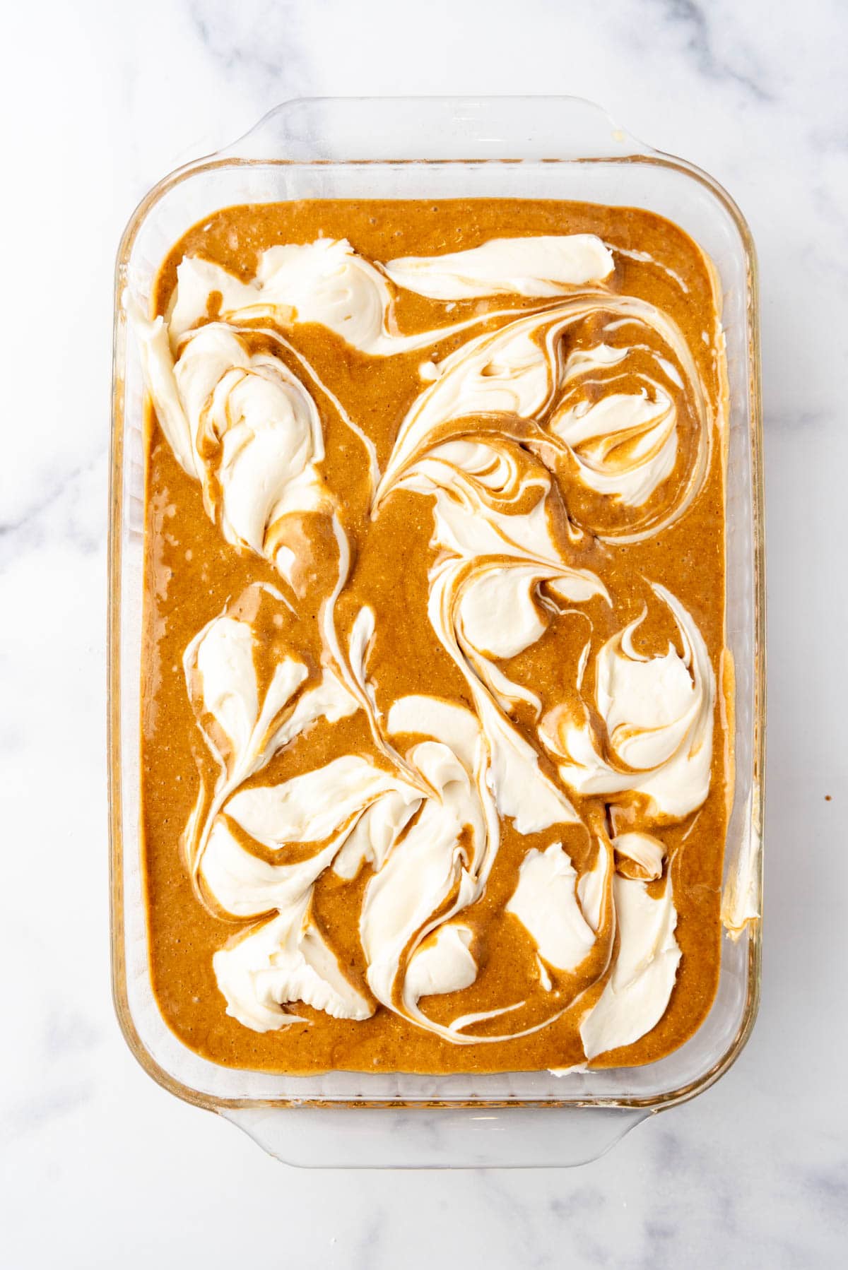 Swirled cream cheese filling in gingerbread cake batter in a baking dish.