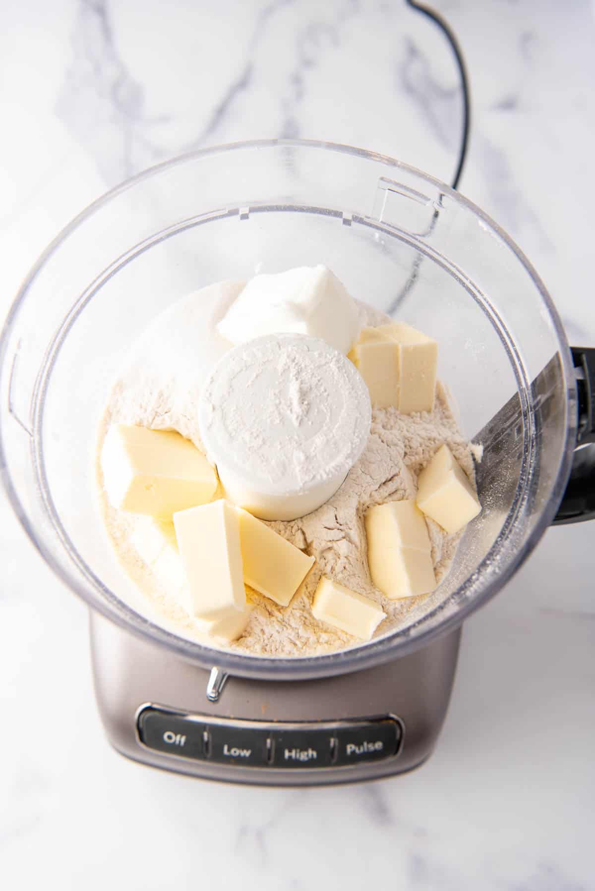 Adding cold cubed butter and shortening to flour, sugar, and salt in a food processor.