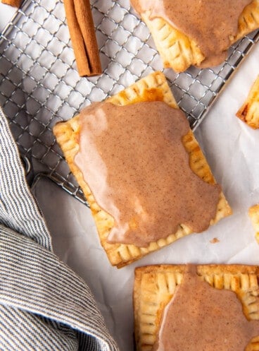 An overhead image of a brown sugar cinnamon pop tart on a wire rack with cinnamon sticks and a linen napkin nearby.