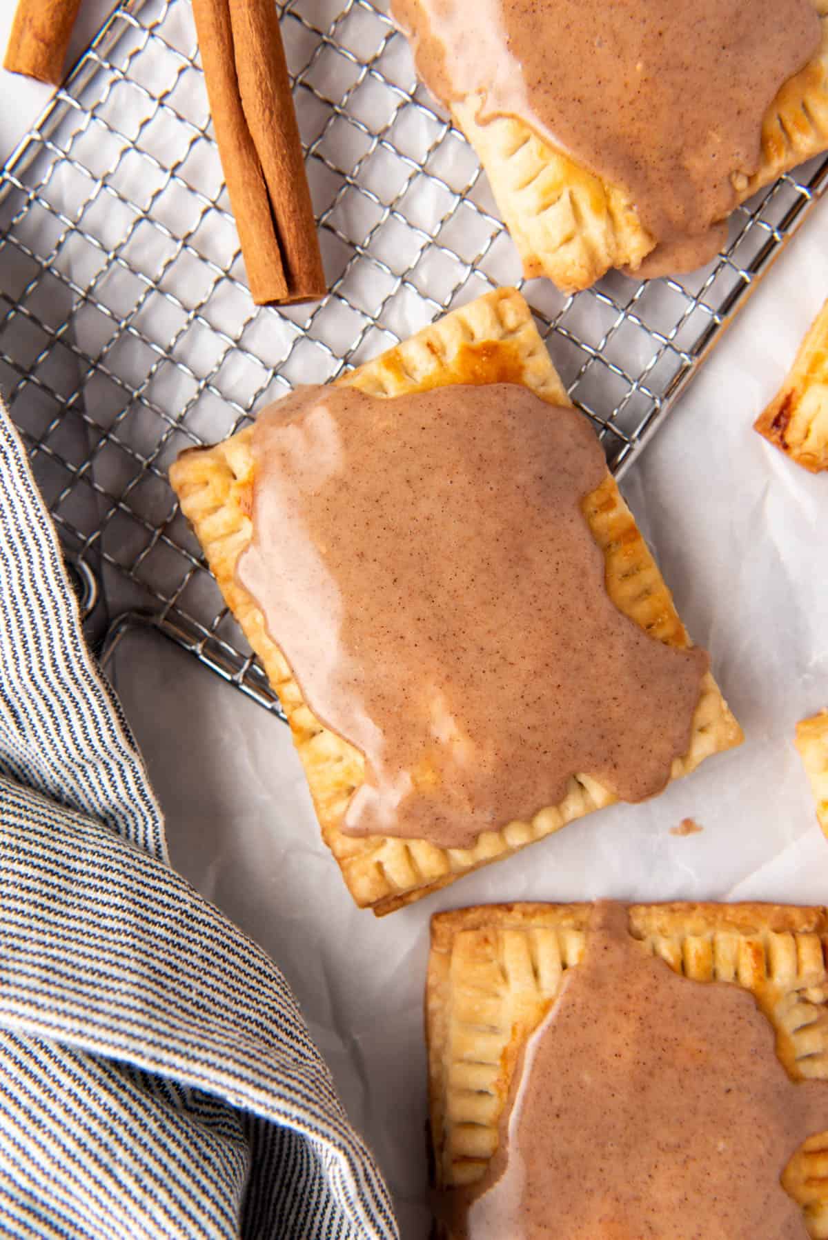 An overhead image of a brown sugar cinnamon pop tart on a wire rack with cinnamon sticks and a linen napkin nearby.
