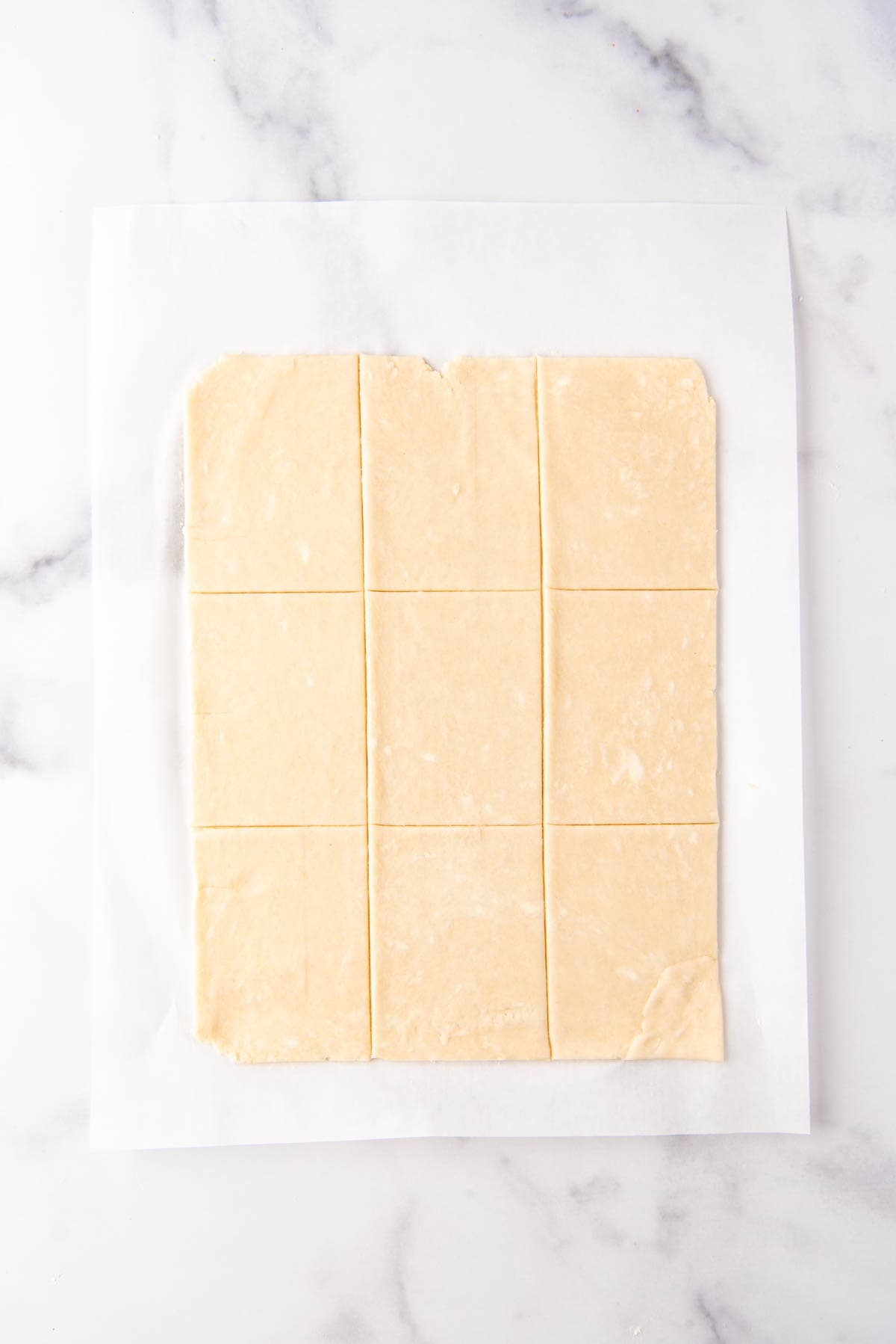 Pie dough trimmed into nine 3x4-inch rectangles on parchment paper.