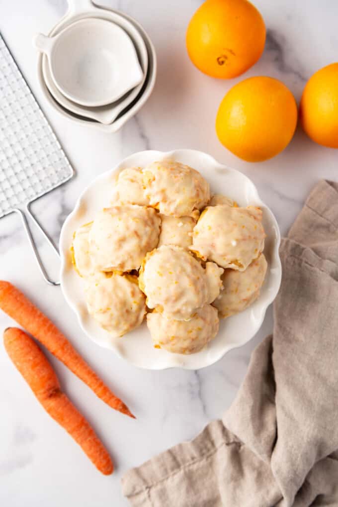 An overhead image of carrot cookies on a white plate surrounded by oranges and carrots.