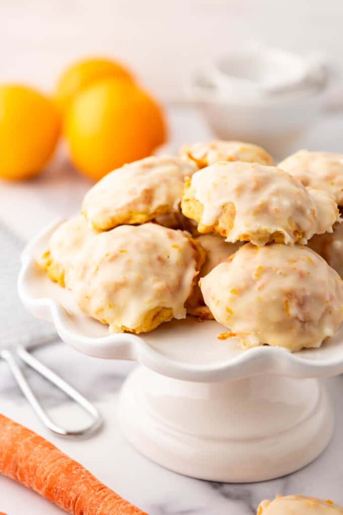 Soft glazed carrot cookies on a white cake stand.