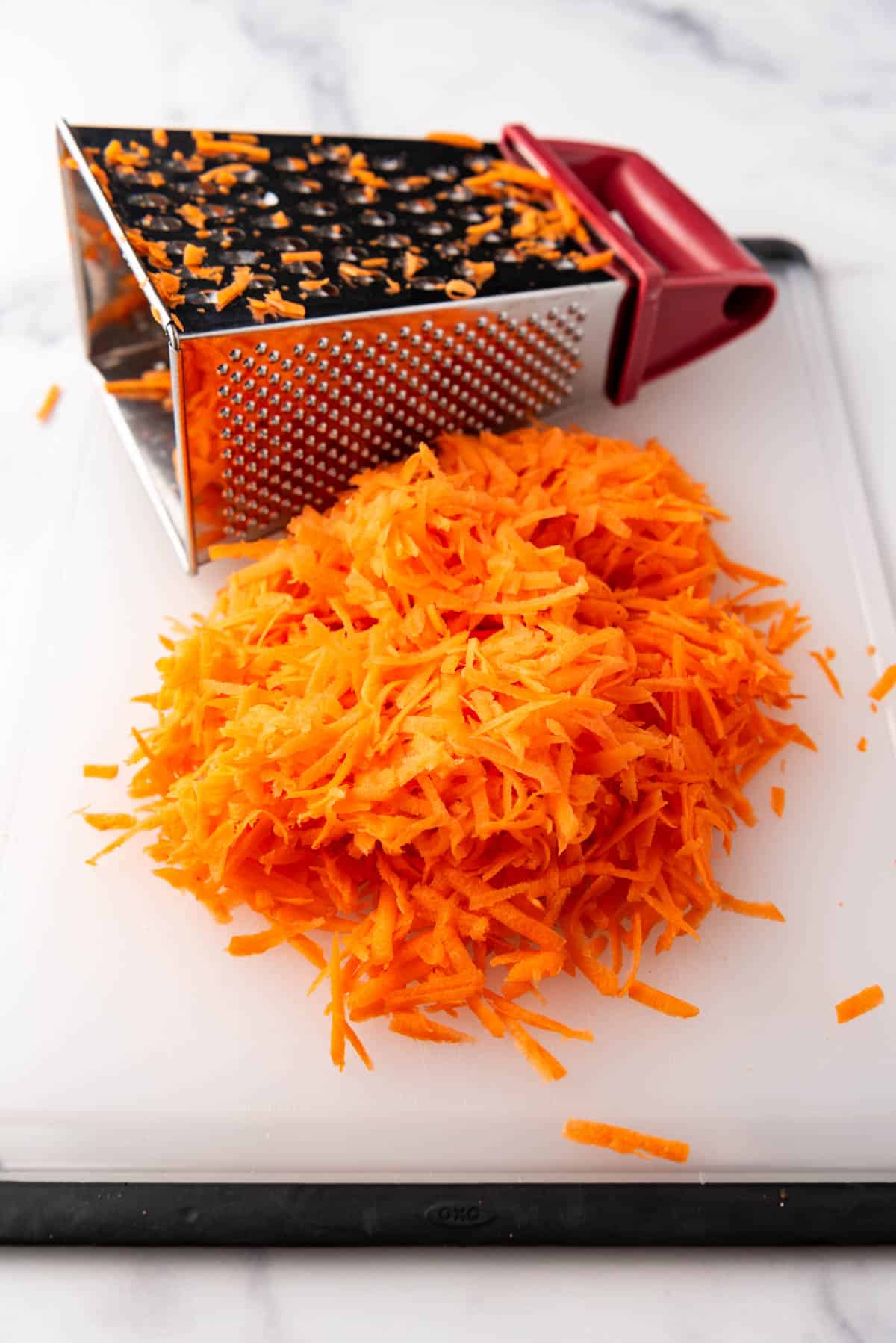 A large pile of shredded carrot in front of a box grater.