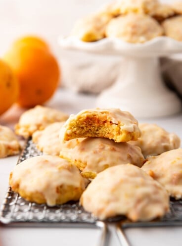 Carrot cookies with orange glazed stacked on top of each other with a bite taken out of the top one.