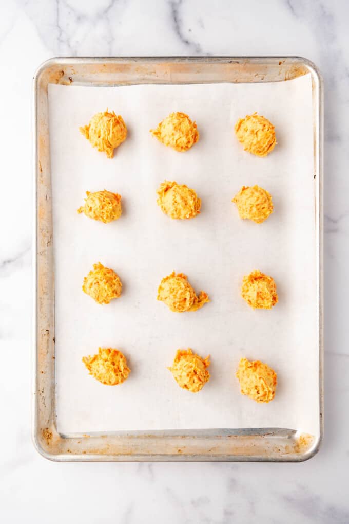 Scooped balls of carrot cookie dough on a baking sheet lined with parchment paper.