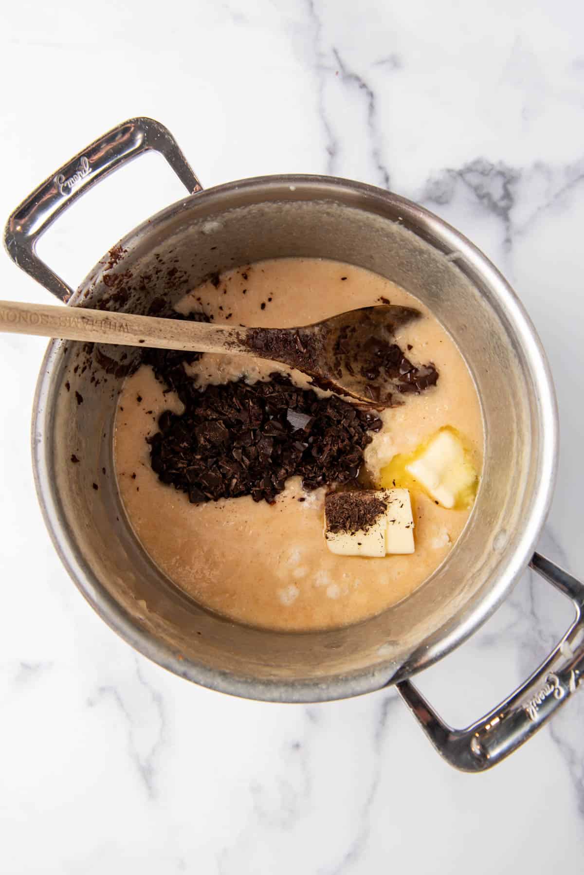Adding chopped dark chocolate and butter to hot sugar and evaporated milk in a large saucepan.