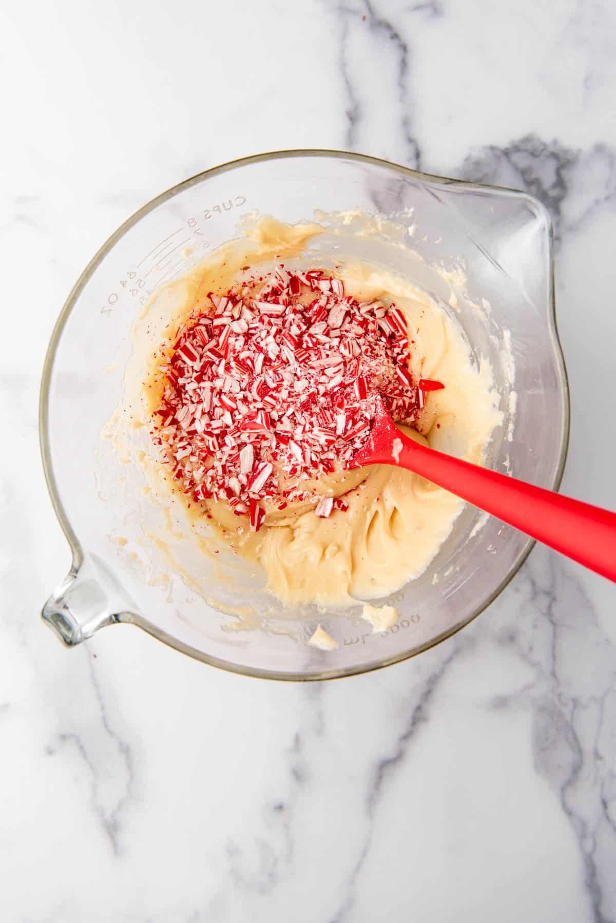 Adding crushed candy cane pieces to white chocolate fudge.