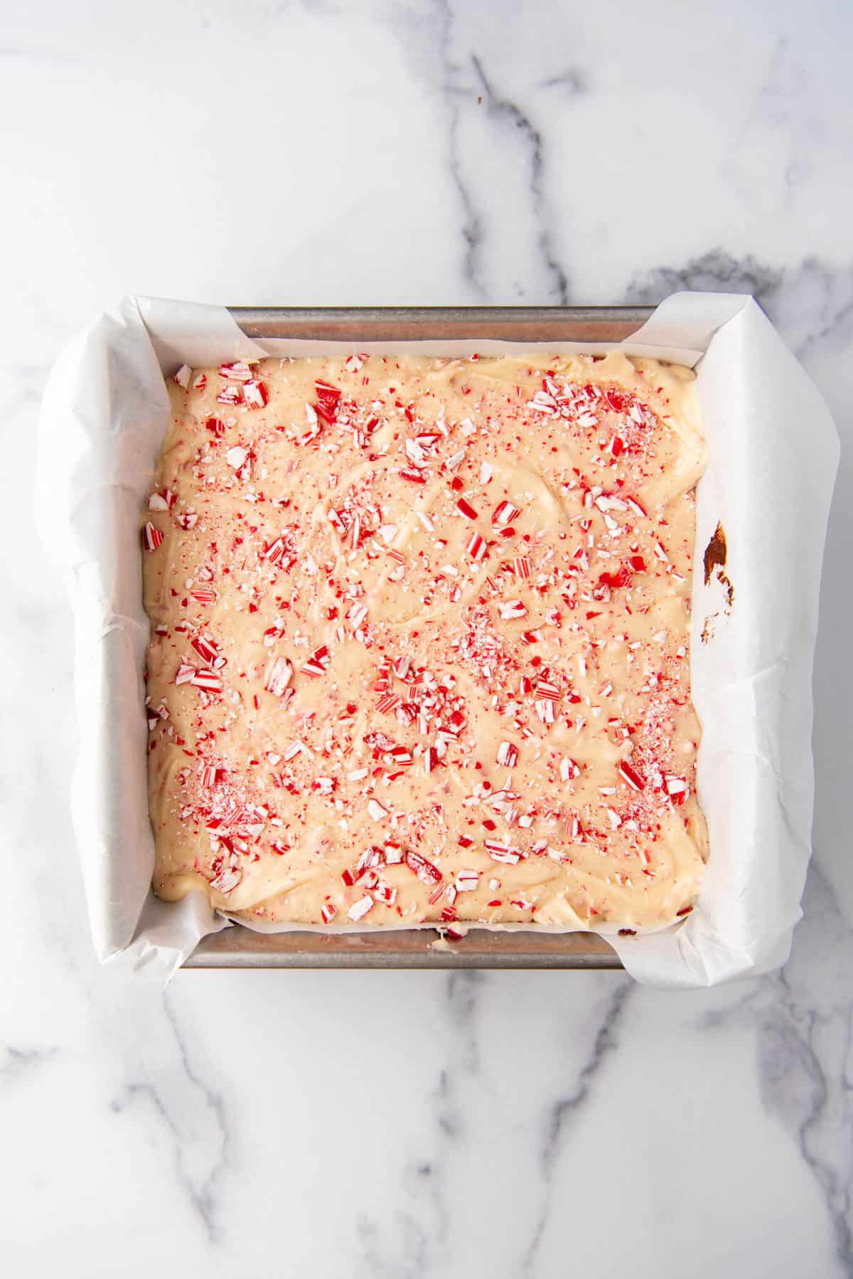 Peppermint bark fudge in a pan with chopped candy cane pieces sprinkled on top.