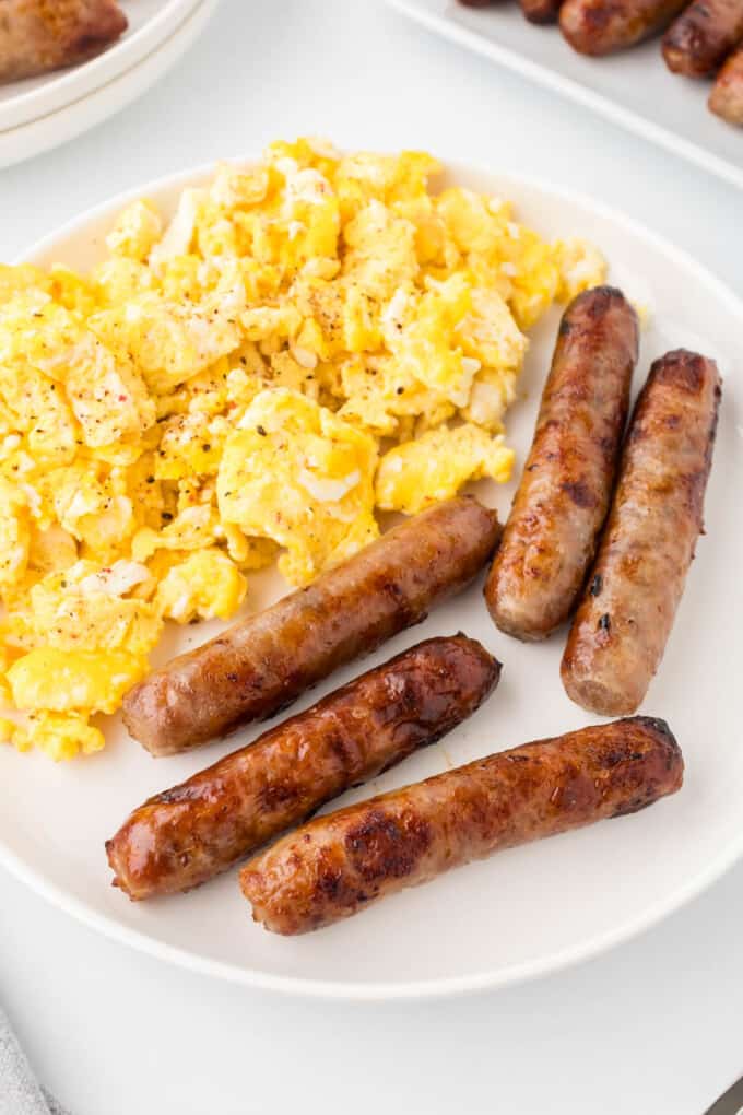 Cooked sausage links on a white plate with scrambled eggs.