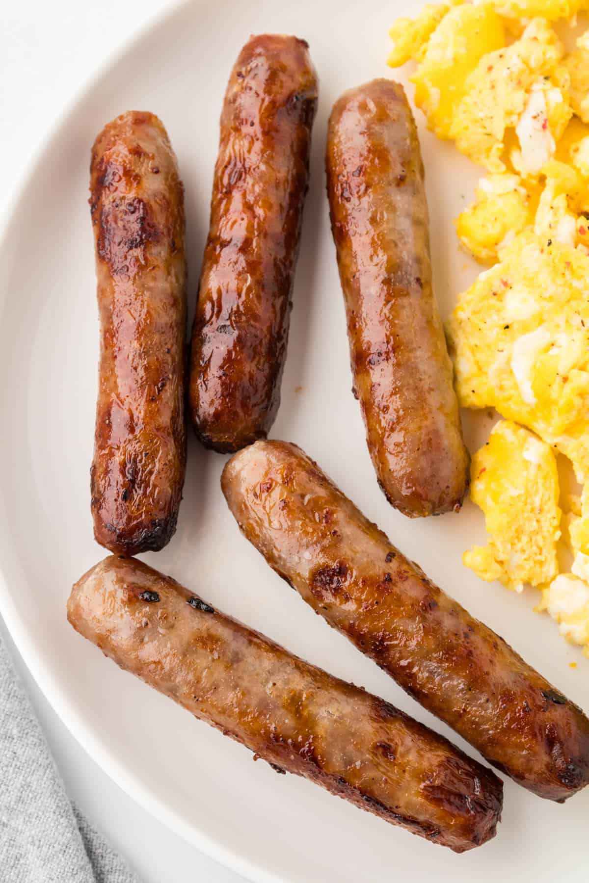 An image of breakfast sausage links on a plate with scrambled eggs.