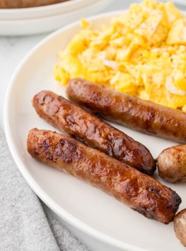 An image of cooked breakfast sausages on a plate with scrambled eggs.