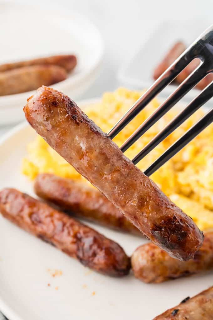 A fork holding up a cooked breakfast sausage.